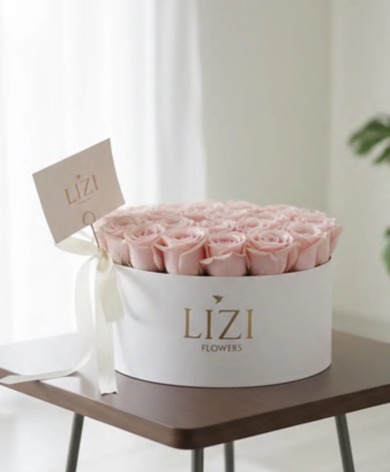Box blanco con rosas rosadas y tarjeta Lizi junto a una ventana